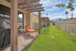 A covered outdoor seating area with a lawn and a view of palm trees and mountains. - Luxury Retreat Club La Quinta- Monthly Condo (La Quinta)
