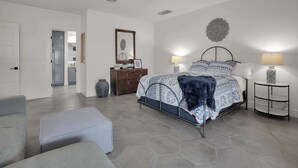 Un dormitorio con cama, dos lámparas de noche, ventilador de techo, cómoda, espejo y un adorno en la pared.