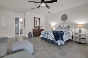 Ein Schlafzimmer mit einem Bett, zwei Nachttischlampen, einem Deckenventilator, einem Schminktisch, einem Spiegel und einem Wandbild.