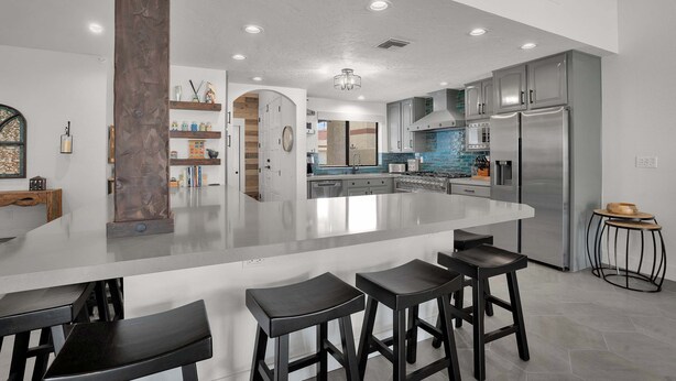Cocina moderna con una isla grande, taburetes de bar, electrodomésticos de acero inoxidable y un salpicadero decorativo.