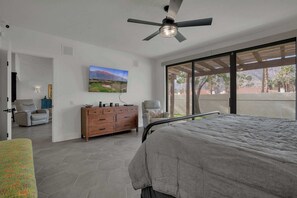 A bedroom with a bed, a dresser, a chair, a ceiling fan, and a large window with a view of palm trees and mountains. - Luxury Retreat Club La Quinta- Monthly Condo (La Quinta)