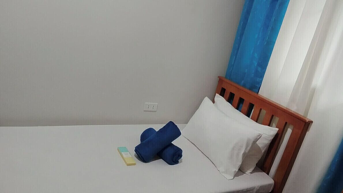 Una cama individual con cabecera de madera, una almohada blanca y toallas azules enrolladas.