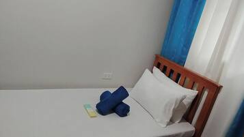 Una cama individual con cabecera de madera, una almohada blanca y toallas azules enrolladas.