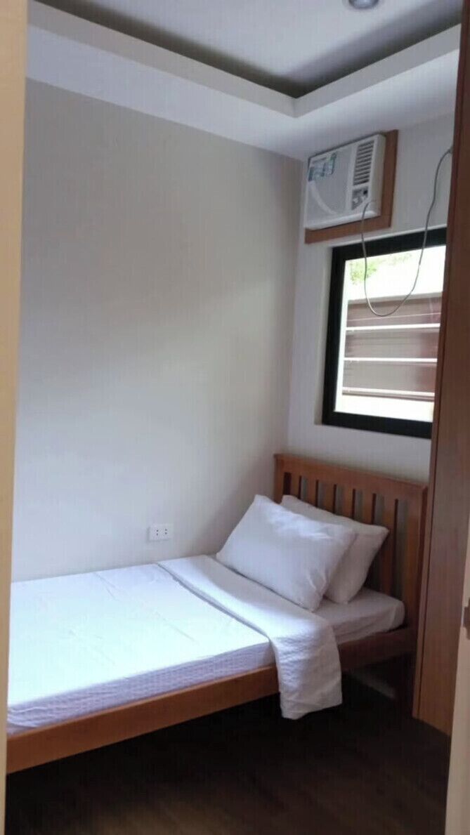 Habitació petita amb un llit individual, un matalàs blanc i una finestra amb persianes.