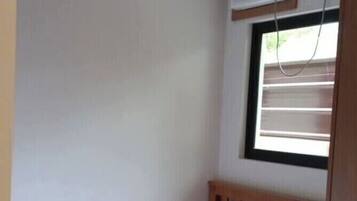 Habitació petita amb un llit individual, un matalàs blanc i una finestra amb persianes.