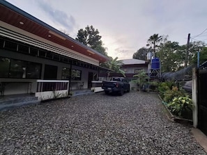 A gravel driveway leading to a building with a red roof and a blue water tank in the background.