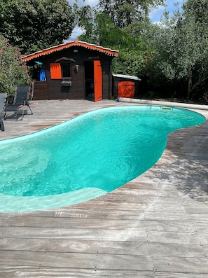 A swimming pool with a wooden deck, a small wooden structure with a red roof, and surrounding greenery. - Villa Marilou: Quiet Location and Private Pool (Cestas)