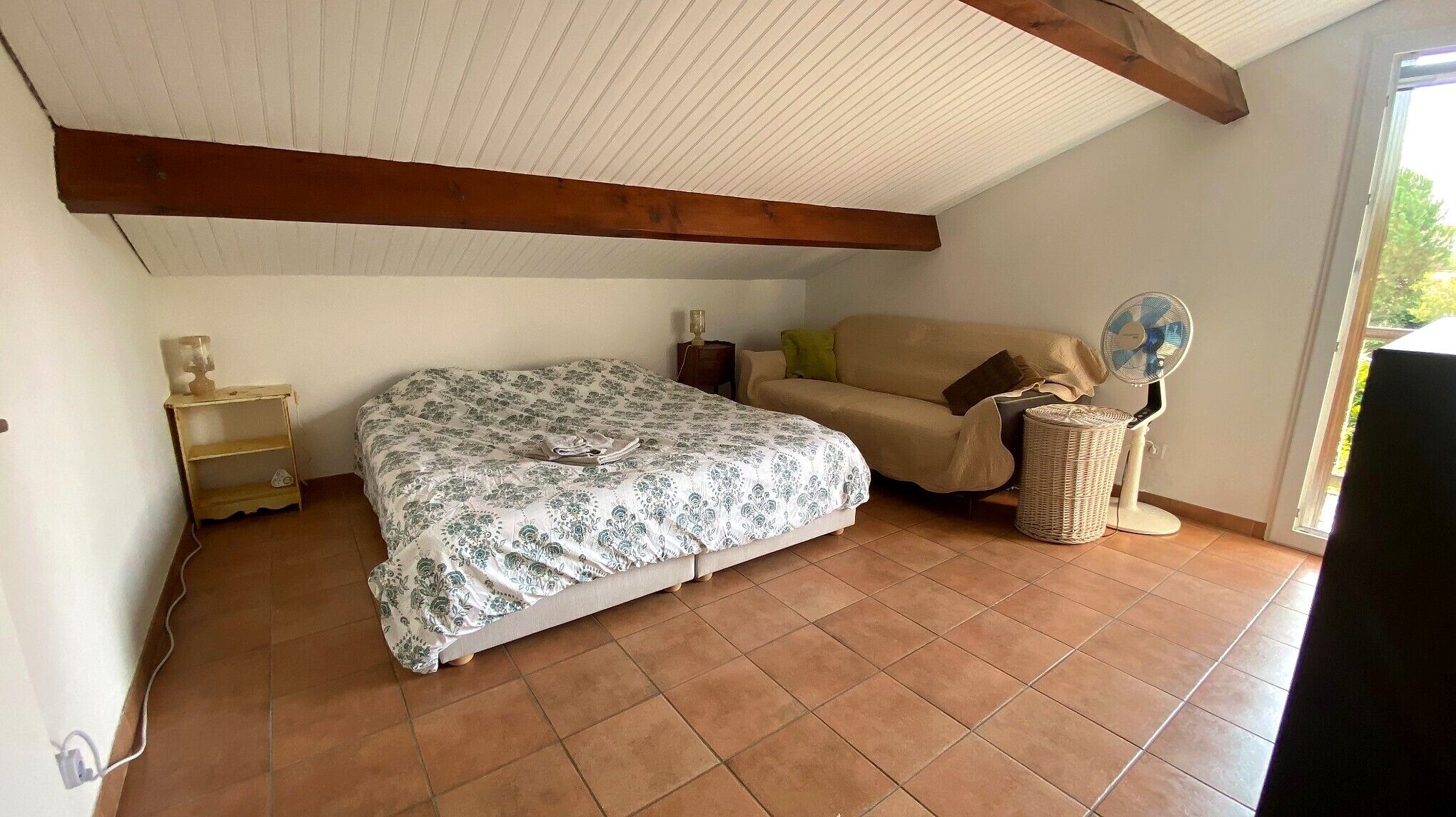 Een slaapkamer met een bed, een bank, een ventilator en een lamp.