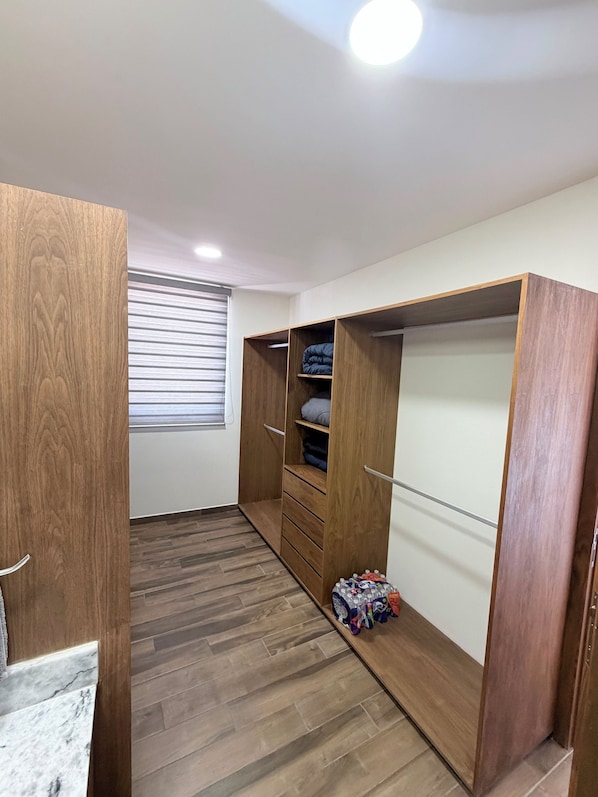 A walk-in closet with wooden doors, a window with blinds, and a tiled floor.