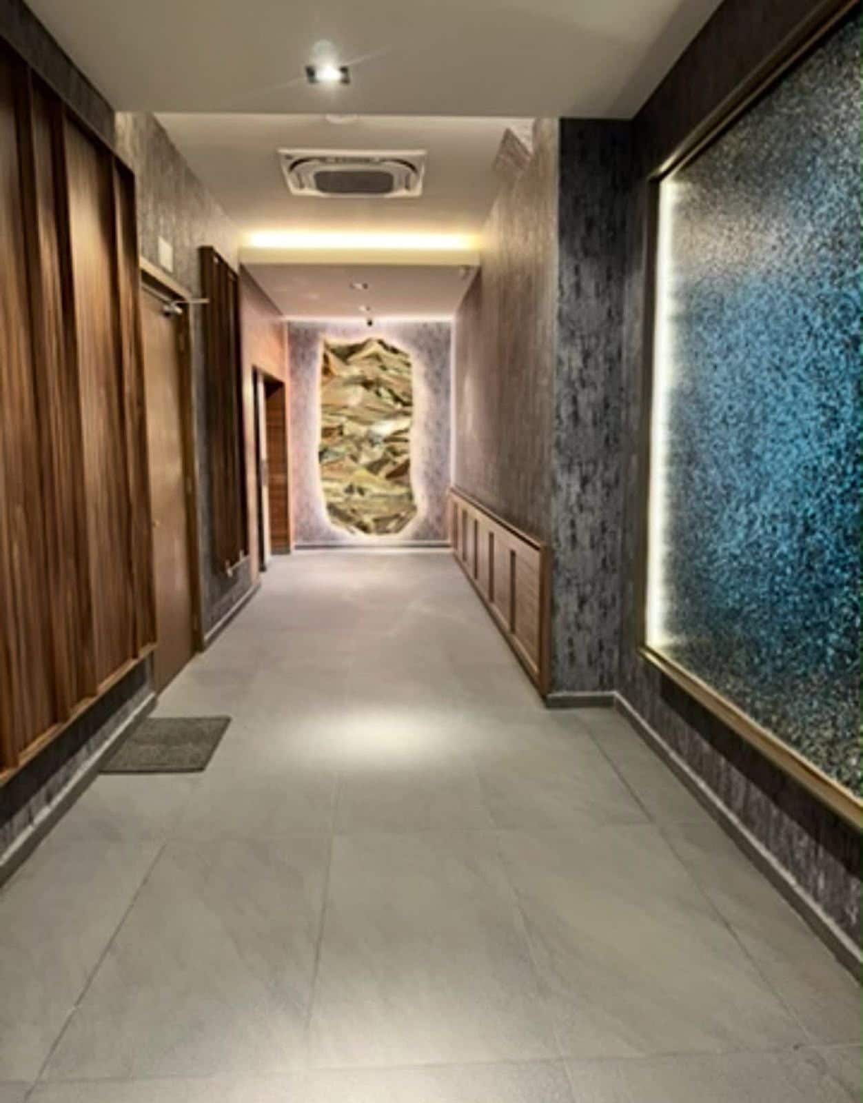A hallway with a wooden door on the left, a textured wall on the right, and a patterned wall at the end.