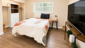 A bedroom with a bed, a TV, a wardrobe, and a window.