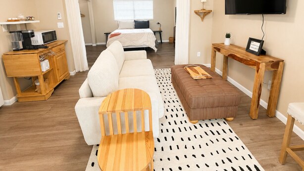 A hotel room with a sofa, a wooden coffee table, a TV, a bedside table, and a bed.
