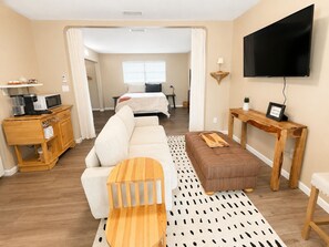 A hotel room with a sofa, a wooden coffee table, a TV, a bedside table, and a bed.
