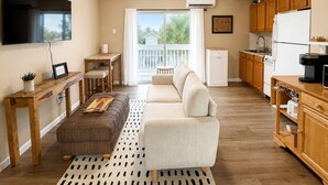 A compact living space with a sofa, ottoman, dining table, and kitchenette.