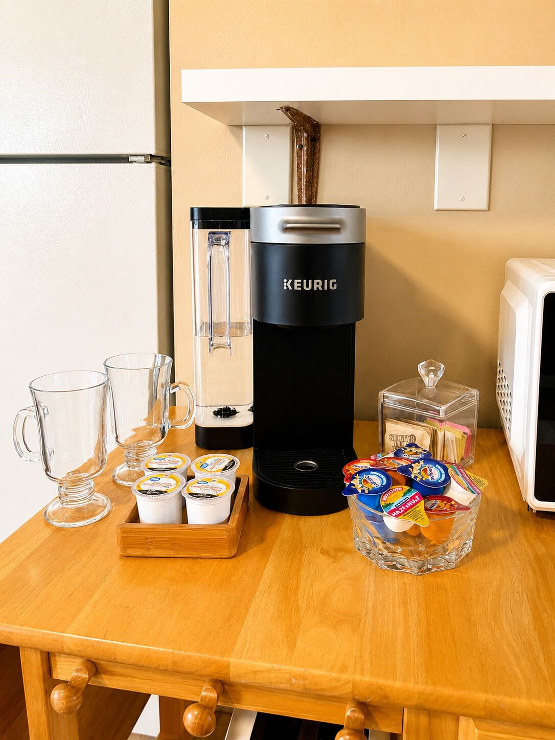 Eine Küchenzeile mit einer Keurig-Kaffeemaschine, einer Mikrowelle, einem Behälter mit Snacks und einer Kaffeemaschine.