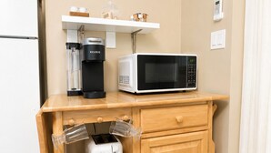 A kitchenette with a coffee maker, microwave, toaster, and a small shelf with cups.