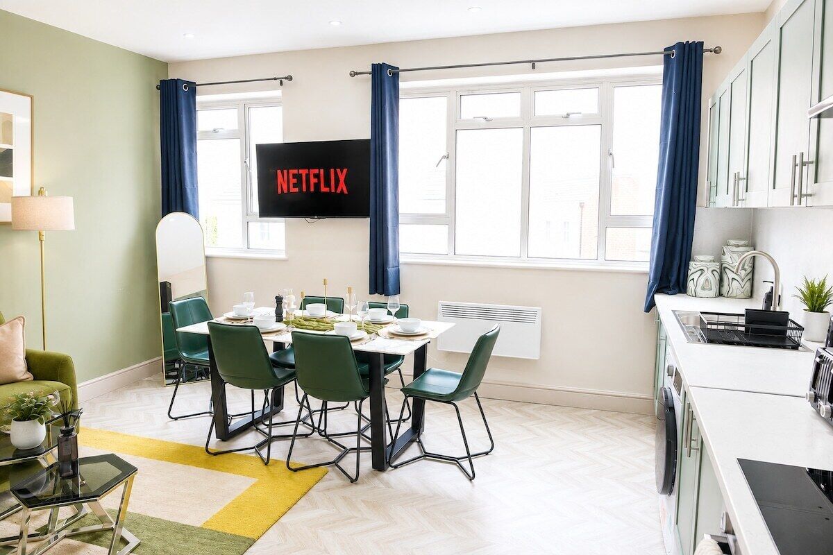 A modern kitchen with a dining area, a TV screen displaying 'NETFLIX,' and a window with curtains.
