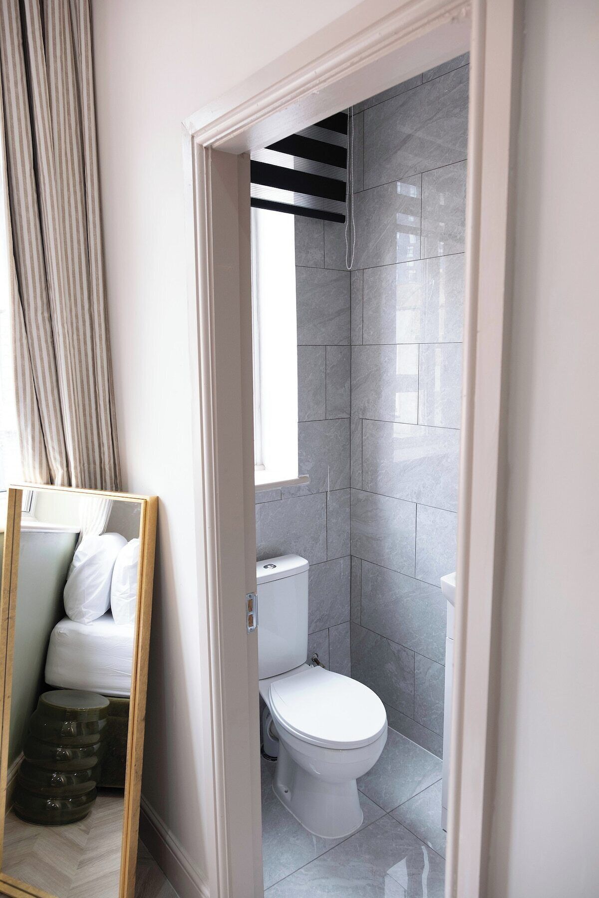 A bathroom with a toilet, a shower area, and a mirror reflecting a bed.