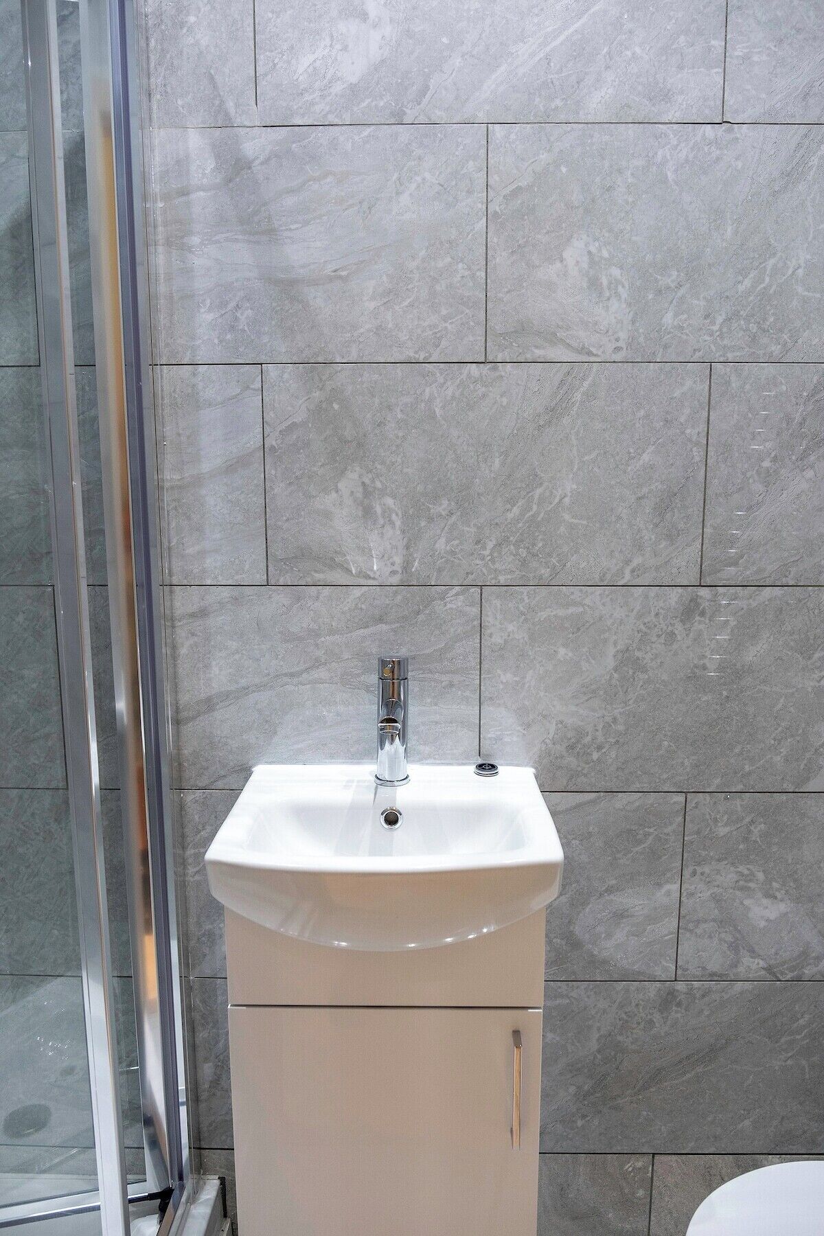 Ein Badezimmer mit einem weißen Waschbecken, einem Chrom-Wasserhahn und einer Duschkabine aus Glas.