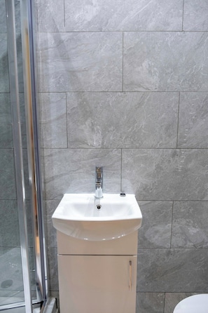 Un bagno con un lavandino bianco, un rubinetto cromato e un box doccia in vetro.