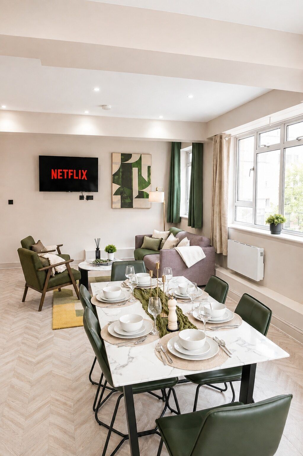 Ein moderner Essbereich mit einem weißen Tisch, gedeckt für sechs Personen, einer Couch und einem Fernseher, der das Netflix-Logo zeigt.
