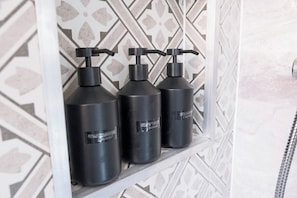 Drei schwarze Flaschen mit Pumpdosierern auf einem Regal vor einer Wand mit Musterung.