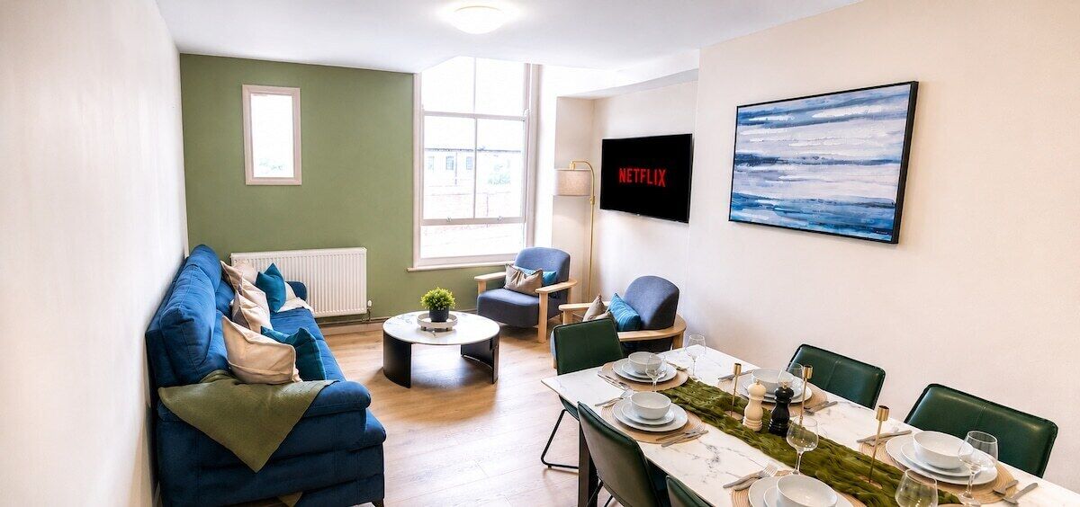 A modern living room with a sofa, a dining table set for four, and a television mounted on the wall.