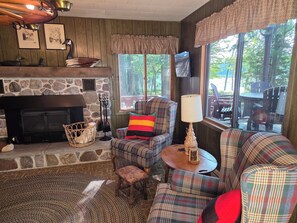 A cozy living room with a fireplace, plaid furniture, and a view of the outdoors.