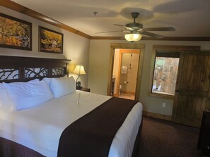 Una camera d'albergo con un letto grande, una ventola a soffitto e vista sull'esterno tramite una porta.