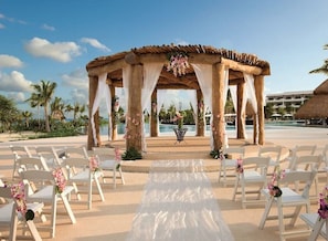 An outdoor wedding ceremony setup with a wooden arch, white chairs, and a white aisle. - All inclusive romantic swim out room with jacuzzi for 2 at Secrets Maroma Beach (Playa del Carmen)