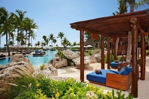 A resort pool area with a wooden gazebo, lounge chairs, and palm trees. - All inclusive romantic swim out room with jacuzzi for 2 at Secrets Maroma Beach (Playa del Carmen)