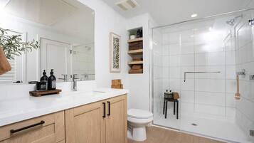 A modern bathroom with a large mirror, wooden cabinets, a white sink, and a glass-enclosed shower.