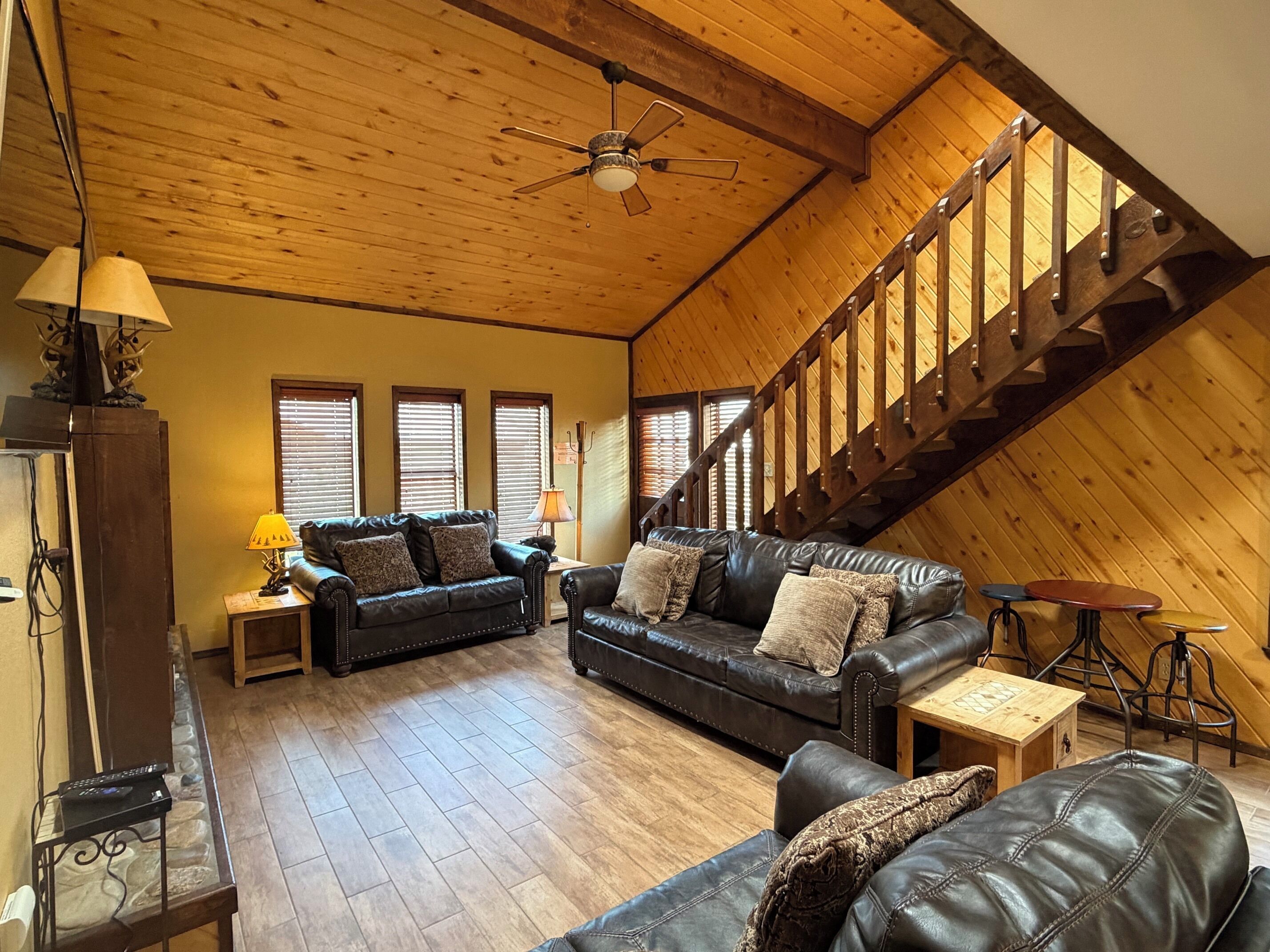 Ein großzügiges Loft mit Holzbalkendecke, einer schwarzen Ledersofa-Garnitur, einem Holzessttisch und einer Treppe.