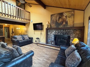 A living room with a fireplace, a television mounted on the wall, and a dining area in the background.