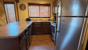 A kitchen with wooden cabinets, a stainless steel refrigerator, and a window with blinds. - Last Chance Cabin in Red River NM (Red River)
