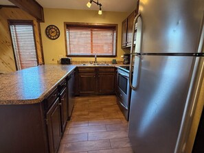 A kitchen with wooden cabinets, a stainless steel refrigerator, and a window with blinds. - Last Chance Cabin in Red River NM (Red River)