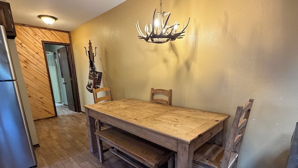 A dining area with a wooden table and chairs, a chandelier, and a refrigerator. - Last Chance Cabin in Red River NM (Red River)