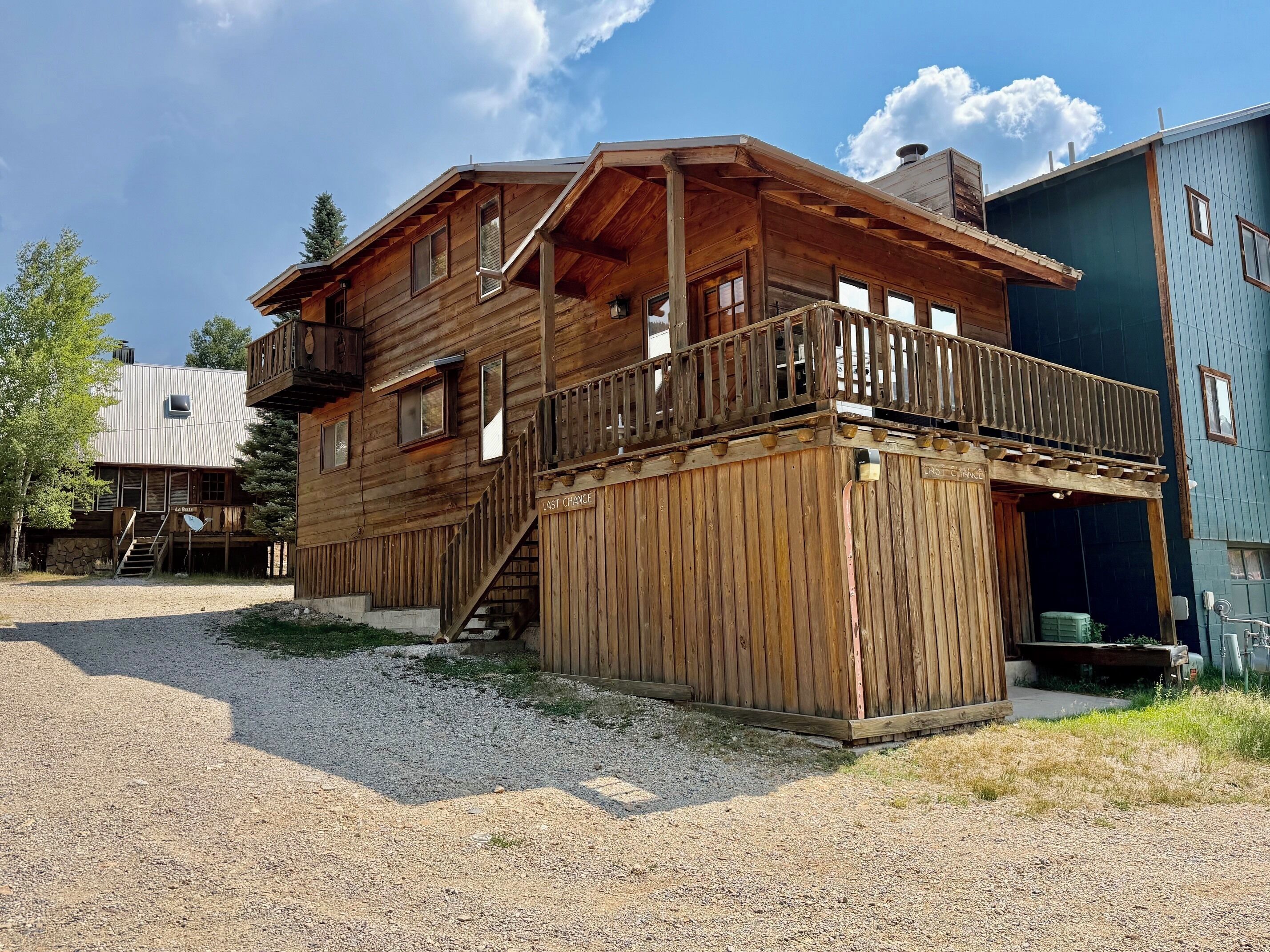 A wooden cabin with a balcony, a staircase, and a gravel driveway.