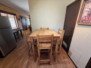 Una mesa de madera para comer con cuatro sillas, un refrigerador y una encimera de cocina con un lavabo.