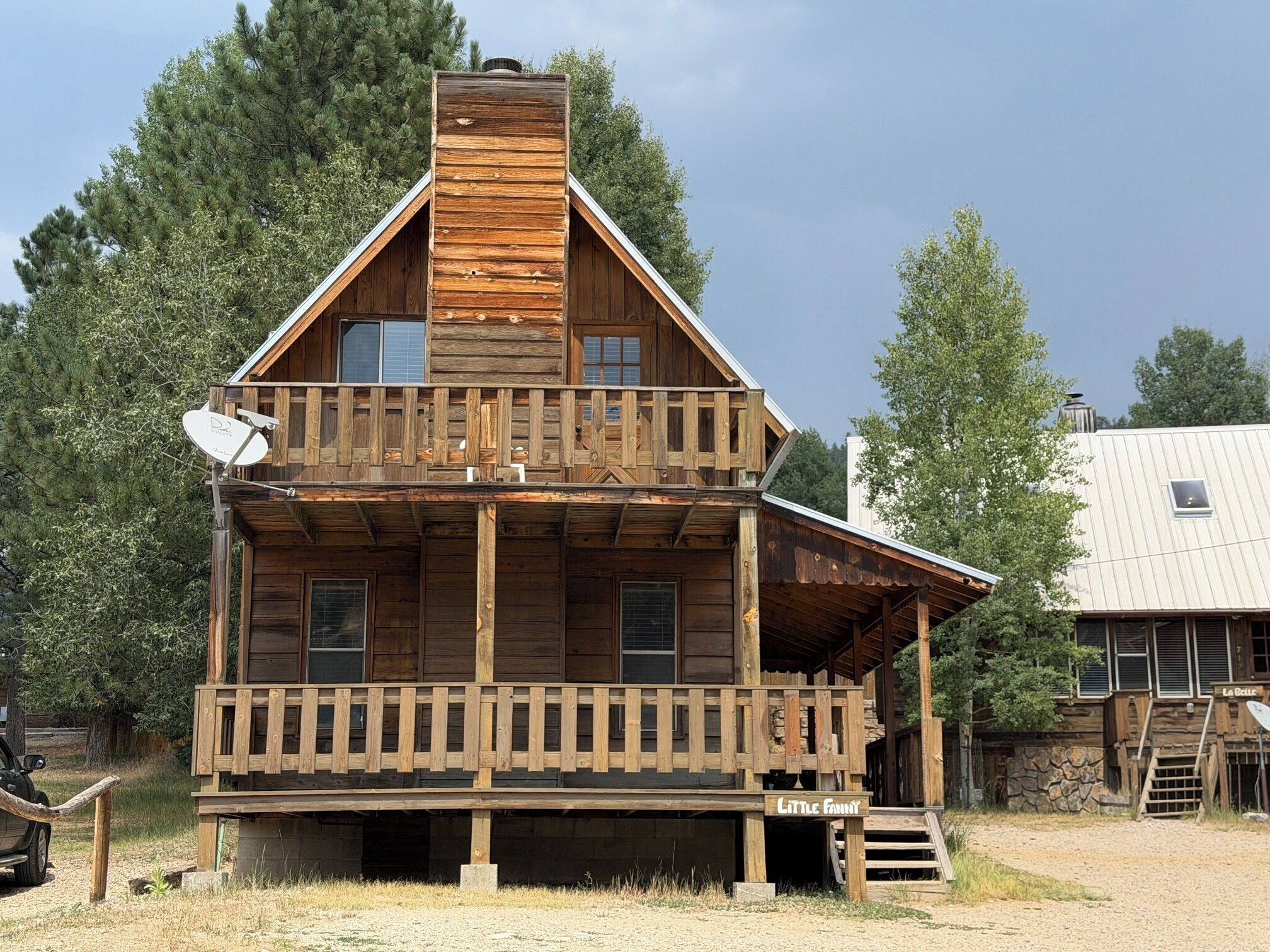A two-story wooden cabin with a balcony, a chimney, and a satellite dish.