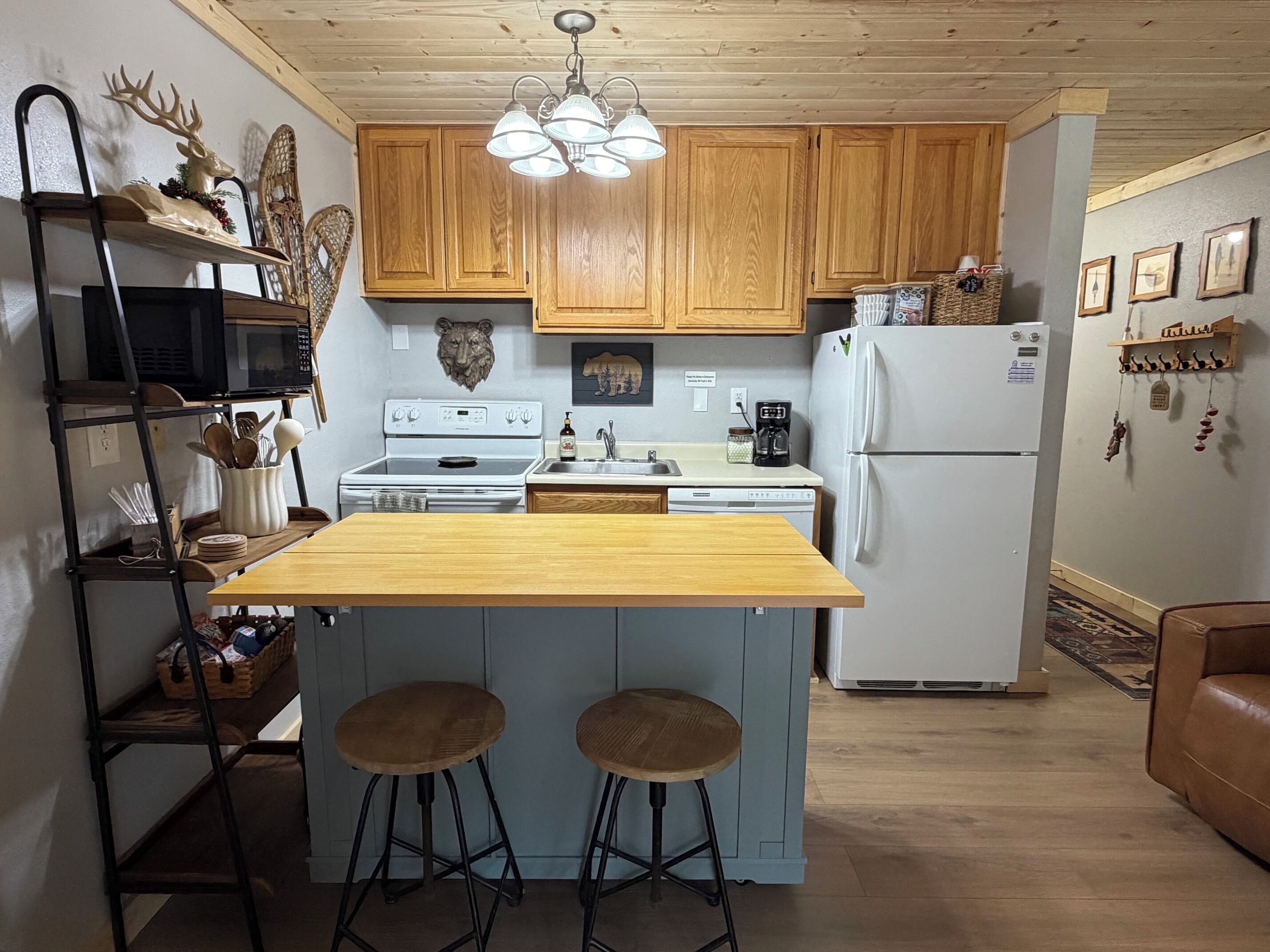 Una cocina con armarios de madera, una isla central con taburetes, microondas, estufa, refrigerador y una araña.