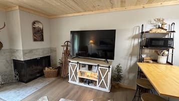 A cozy living room with a fireplace, a television, and a wooden ceiling.