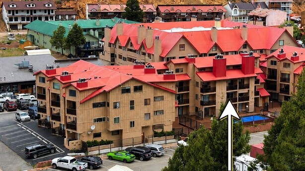 A multi-story hotel with red roofs, a parking lot, and a mountainous backdrop. - Lifts West #109, Williams Peak Retreat (Red River)