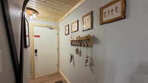 A hallway with wooden ceiling, a door with a red sign, and wall-mounted hooks with items. - Lifts West #109, Williams Peak Retreat (Red River)