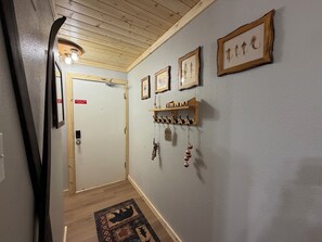 Un pasillo con techo de madera, una puerta con un letrero rojo y ganchos en la pared con objetos.