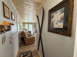 Una sala de estar acogedora con chimenea, un cuadro con temática de esquí y techo de madera.