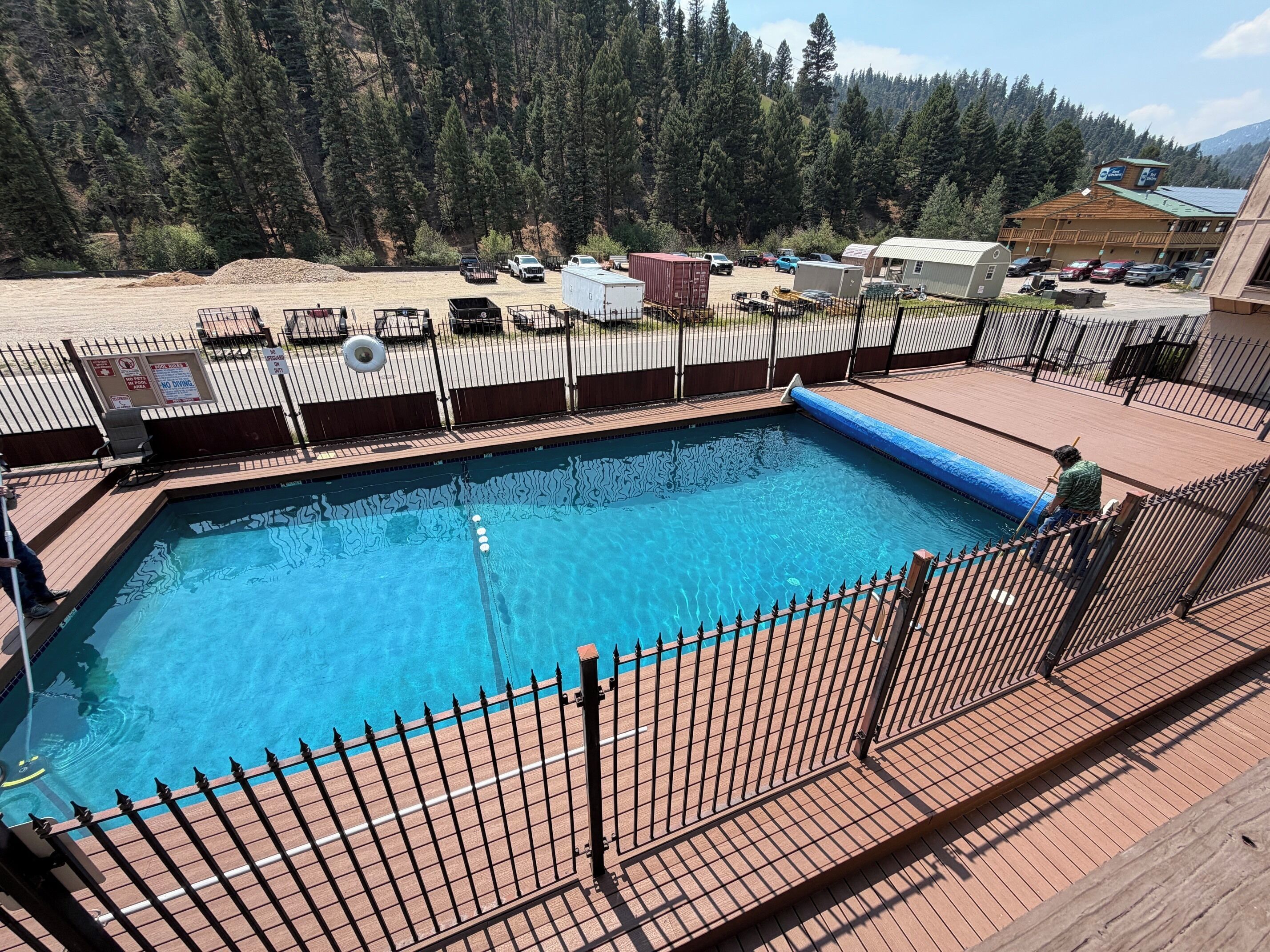 A swimming pool with a wooden deck and a metal fence, surrounded by a mountainous landscape.