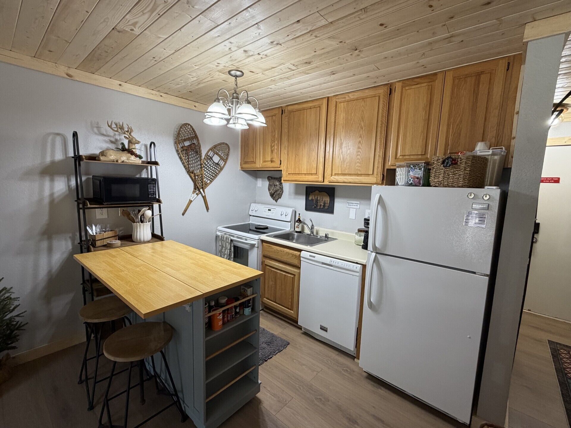 Una cucina compatta con mobili in legno, un frigorifero bianco, un forno a microonde, un fornello e un lavello.