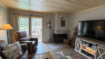 A cozy living room with a leather sofa, a television, a fireplace, and a mounted deer head.