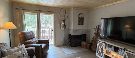 Una sala de estar acogedora con un sofá de cuero, un televisor, una chimenea y una cabeza de ciervo montada.